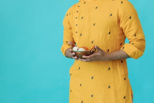Person in Yellow Long Sleeves Carrying a Bronze Bowl with Food 