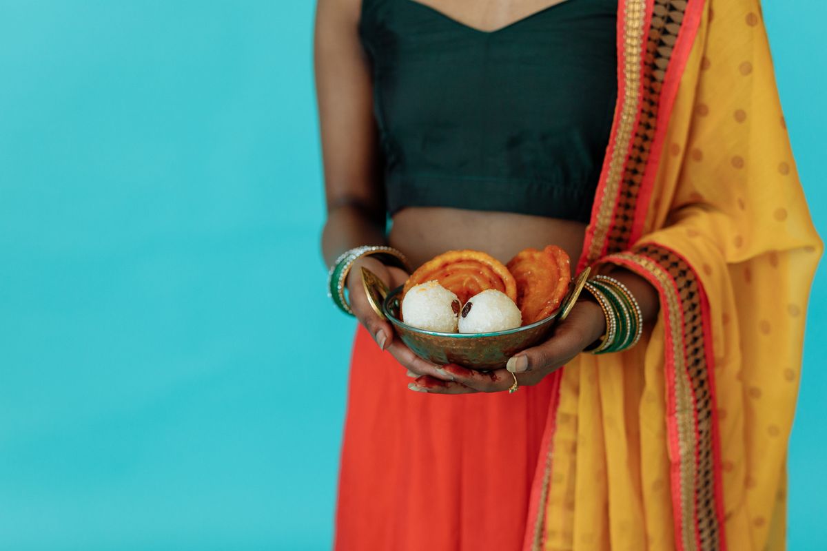 Close-up of woman holding a bowl of traditional Indian sweets in vibrant attire.