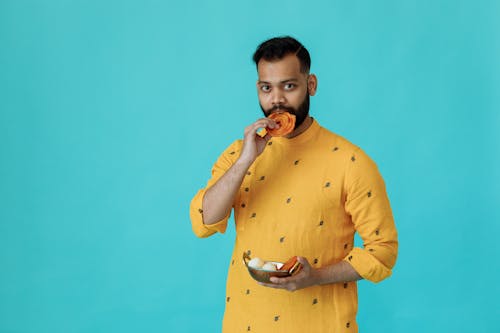 Man in Yellow Traditional Clothes Eating Traditional Food while Looking at the Camera