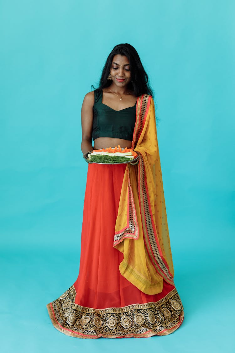 A Woman Wearing A Sari Holding A Plate Of Sliced Vegetables