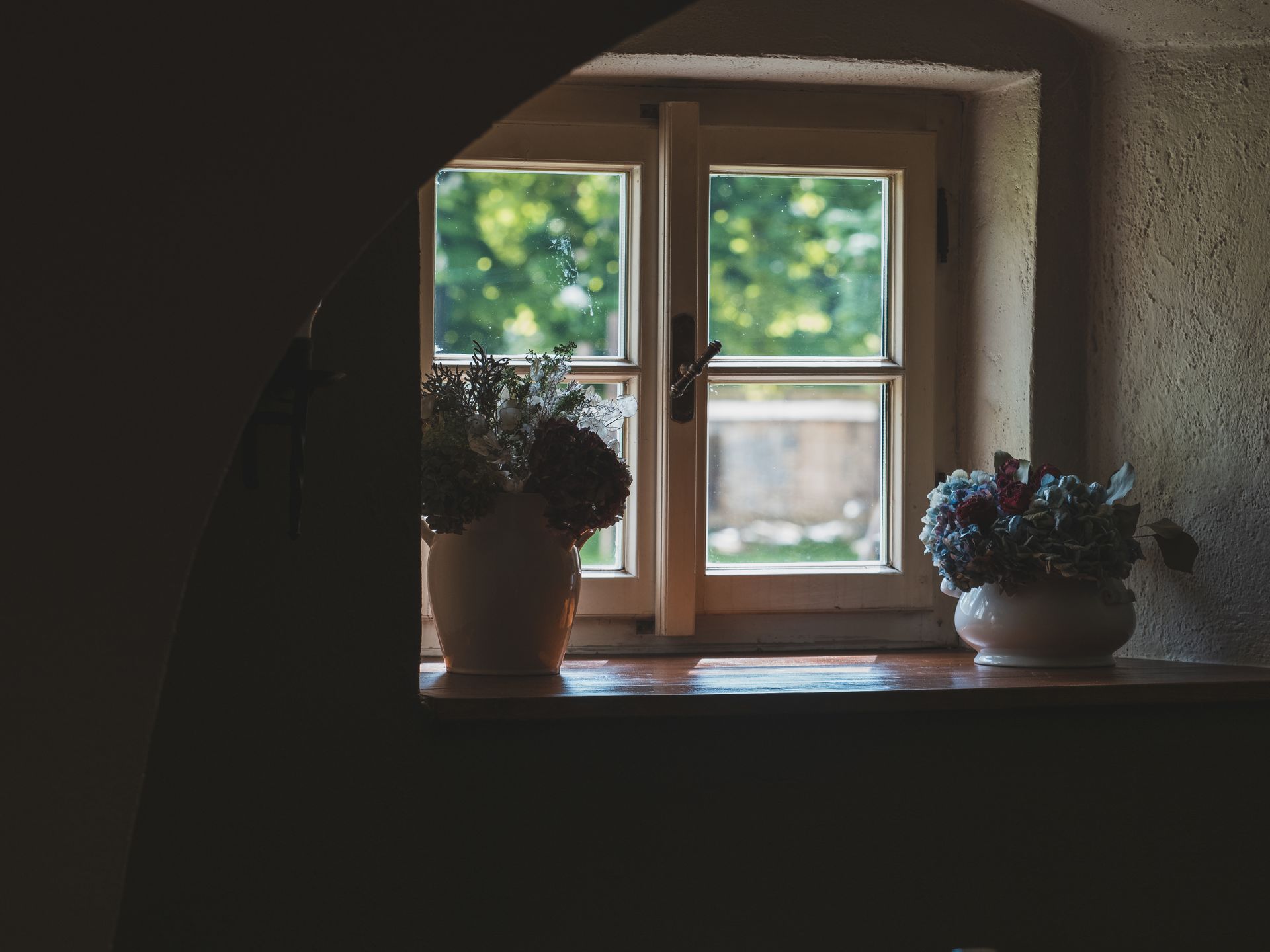 Warm indoor setting with vases of flowers by a wooden window, capturing natural light.