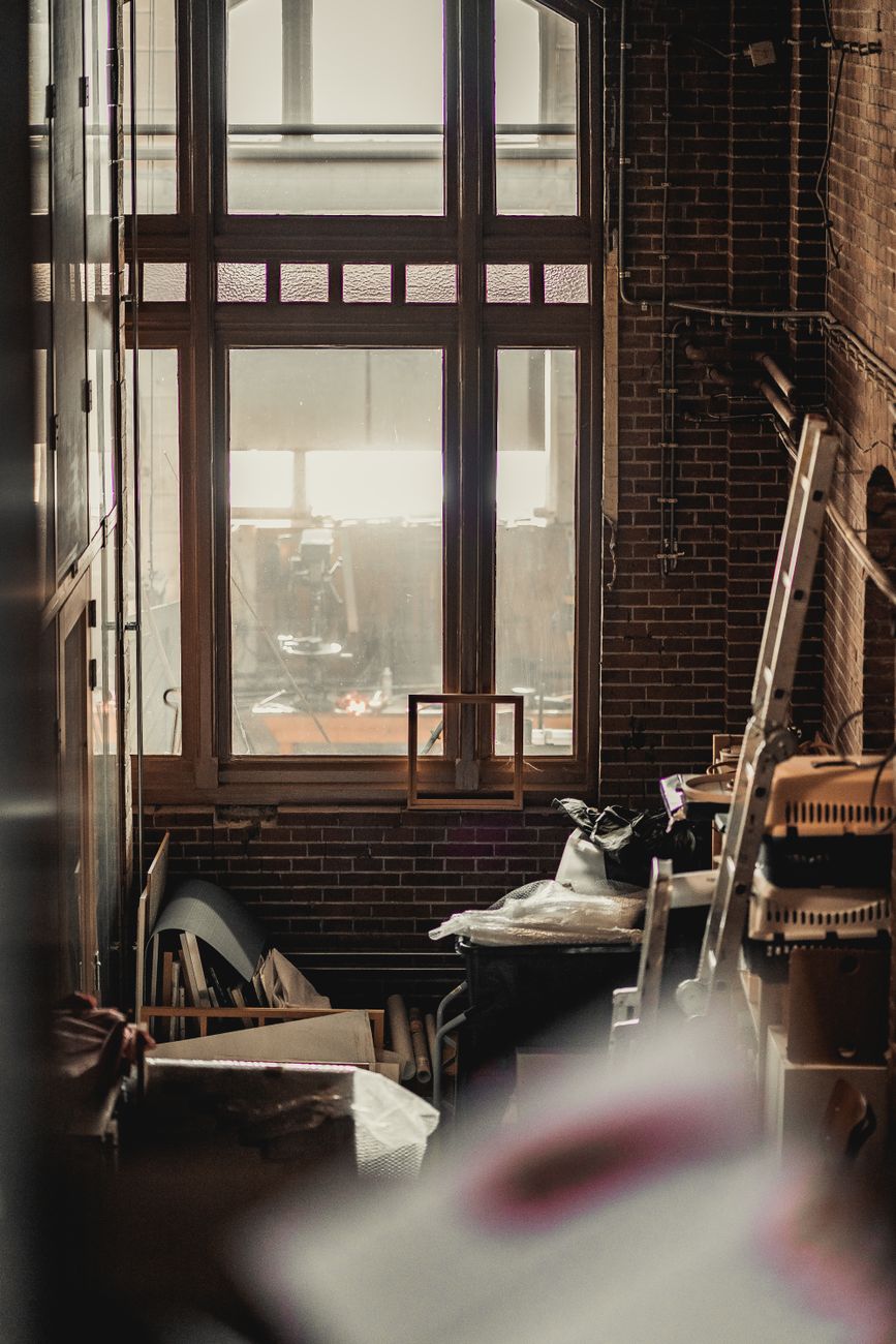 Cluttered industrial-style room featuring a large window and brick walls.. cluttered, industrial, style