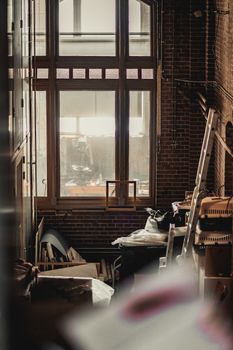 Cluttered industrial-style room featuring a large window and brick walls.. cluttered, industrial, style