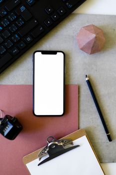 Flat lay of a minimalist workspace featuring a smartphone with blank screen, clipboard, and accessories.