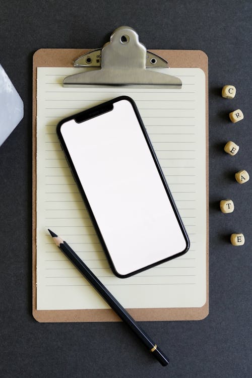Free A Pen and a Cellphone over a Paper on a Clipboard Stock Photo