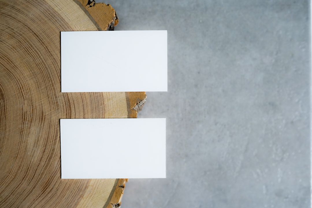 Two blank business cards on a wooden slice and concrete background, minimalistic top view.