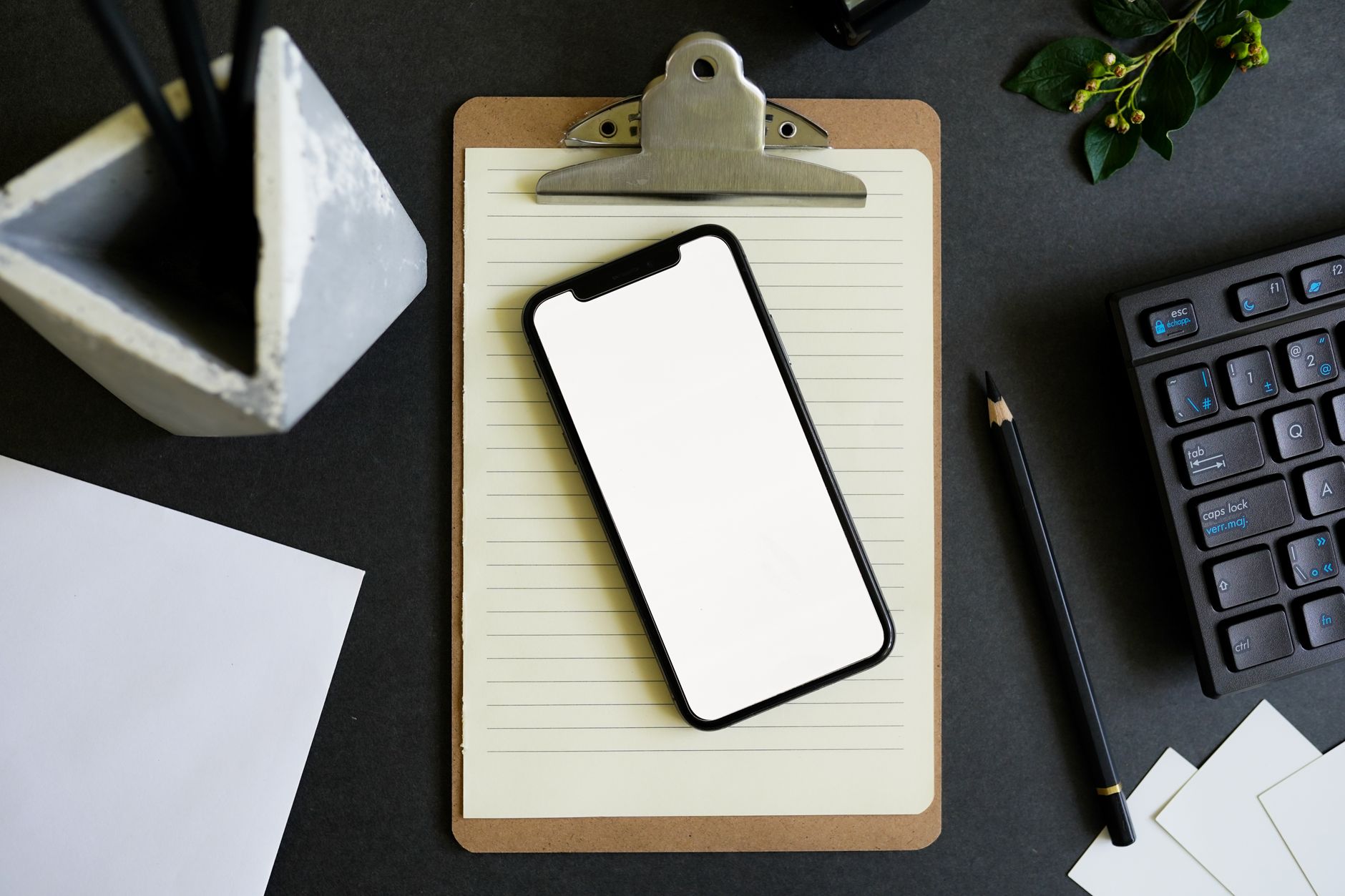 A smartphone on a clipboard in a modern workspace setting with a keyboard and stationery.