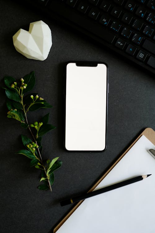 Close-Up Shot of a Mobile Phone beside a Keyboard and Black Pencil 