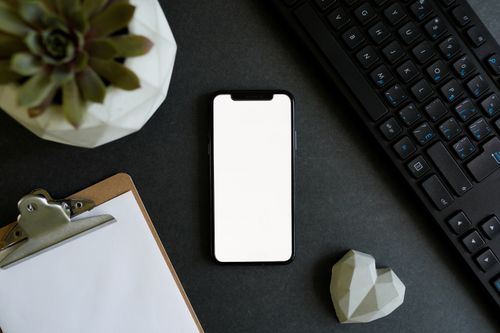 Free Top view of a smartphone, keyboard, succulent plant, and clipboard on a black desk. Stock Photo