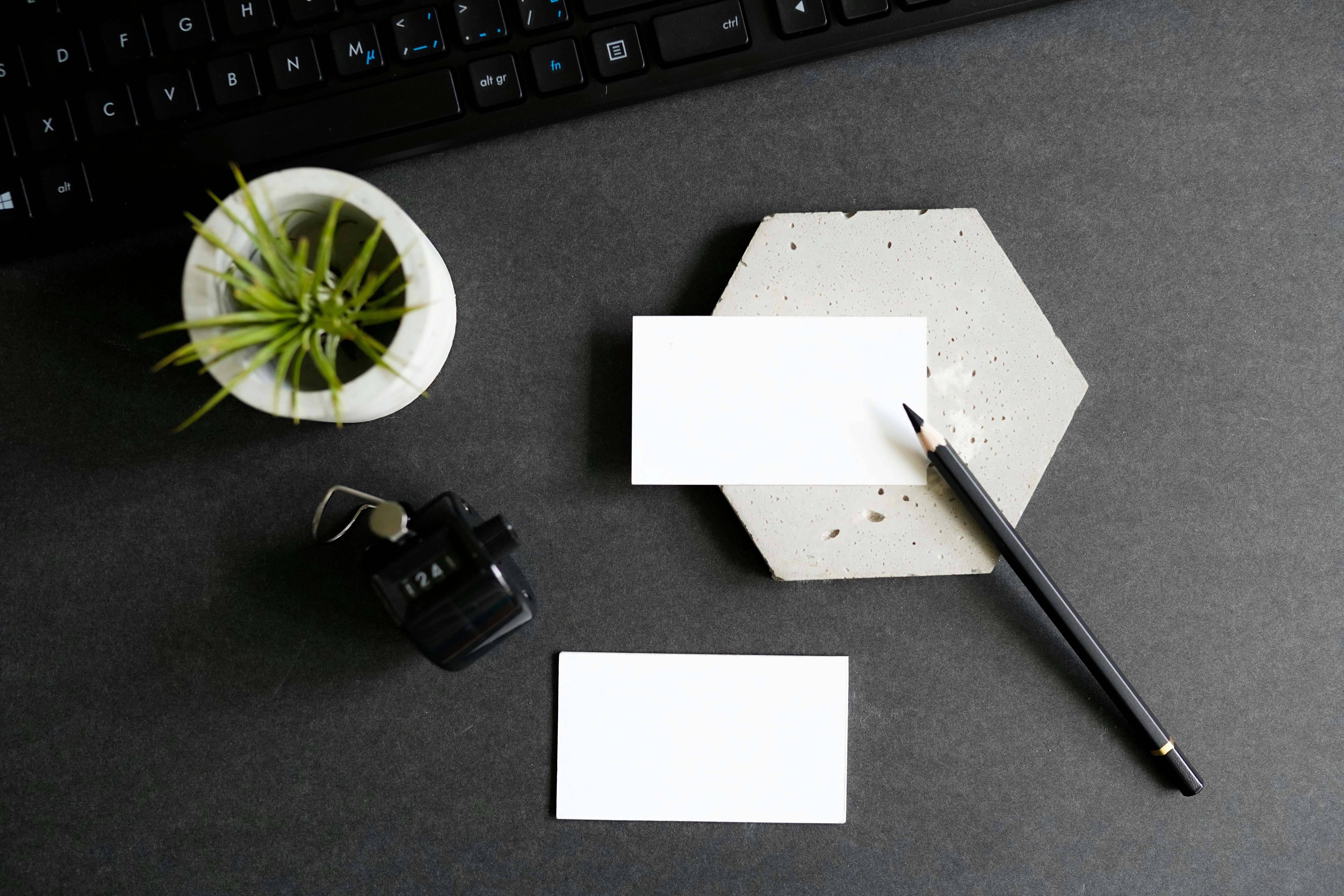 Top view of a stylish office desk setup featuring business cards, keyboard, pencil, and a small houseplant.