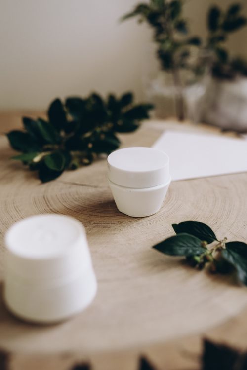 Free Simple still life featuring white containers on a wooden surface with green leaves. Stock Photo
