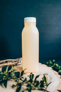 A clean, minimalist bottle placed on a wooden surface with greenery, perfect for product mockups.