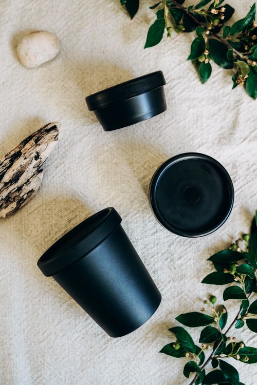 Free Top view of black containers placed on textured fabric with surrounding green foliage. Stock Photo