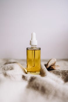 Close-up of a glass serum bottle with yellow liquid on woven fabric, showcasing elegance and simplicity.