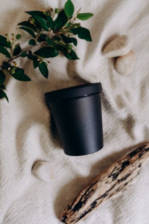 Free A black container on beige fabric with leaves and stones, captured in a minimalist style. Stock Photo