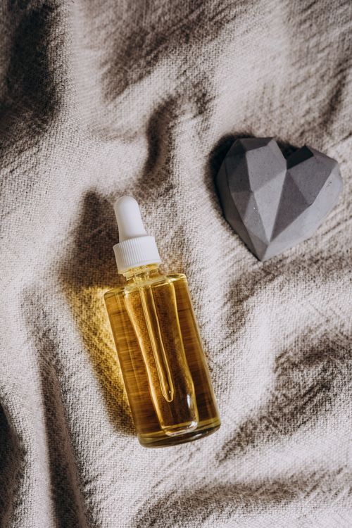 Free Glass dropper bottle of oil placed on textured fabric with a geometric stone heart. Stock Photo