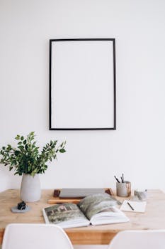 A minimalist home office setup with a blank frame, wooden desk, and decorative plant.