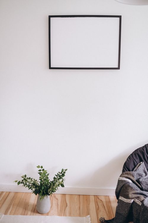 Free A minimalist room featuring a blank frame on a white wall, a vase, and cozy decor elements. Stock Photo