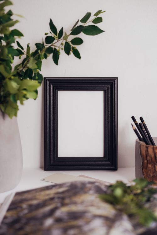 Free Minimalist black frame with greenery on a bright desk setting. Stock Photo