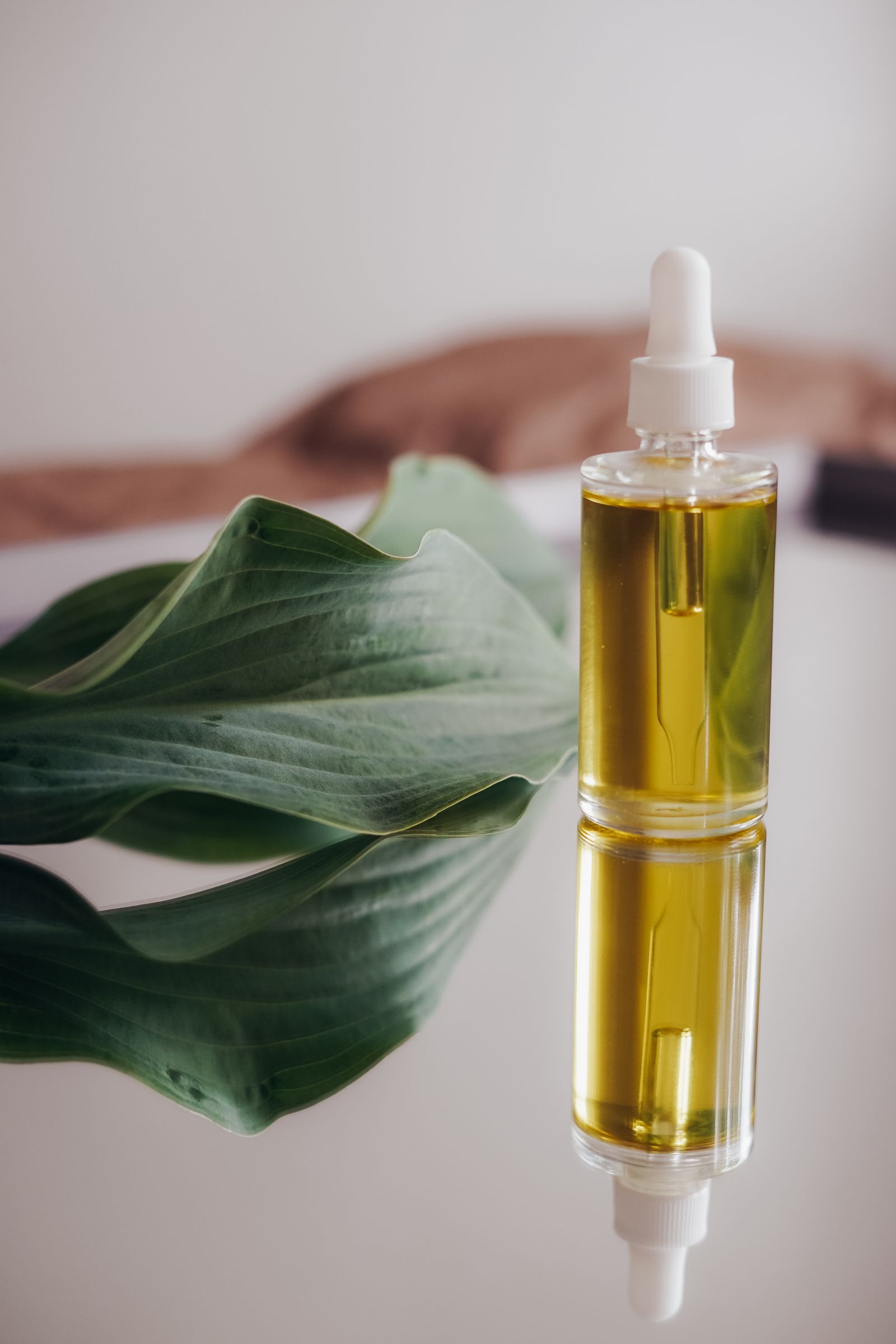 A glass serum bottle with a dropper, a green leaf reflected in the glass