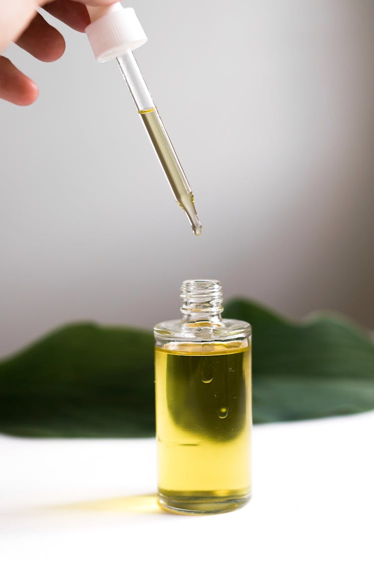 Hand Holding Pipette With Oil From Bottle