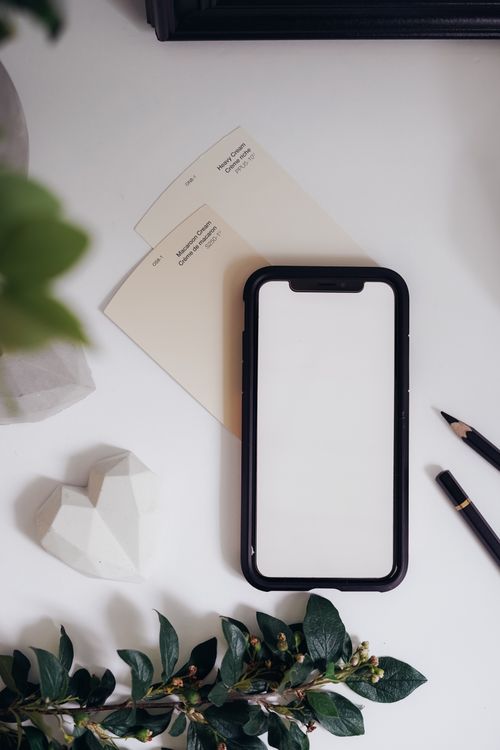 Free A flat lay featuring a blank smartphone screen with pencils, greenery, and decor on a white desk. Stock Photo