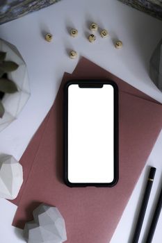 Stylish flatlay showcasing a smartphone, geometric decor, and stationary for creative workspaces.