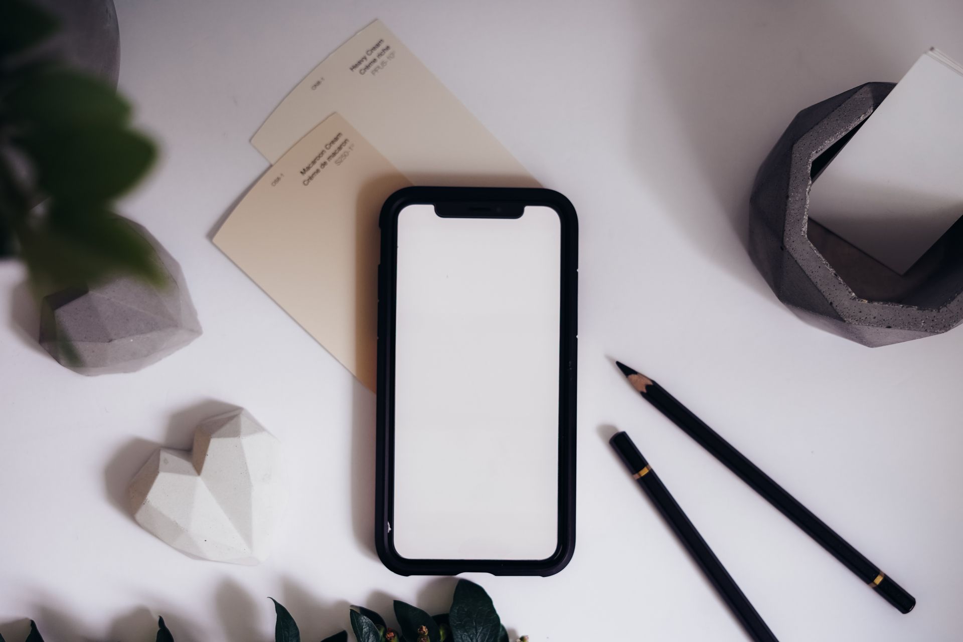 Flat lay of modern desktop with smartphone mockup, pencils, and decor against a clean background.