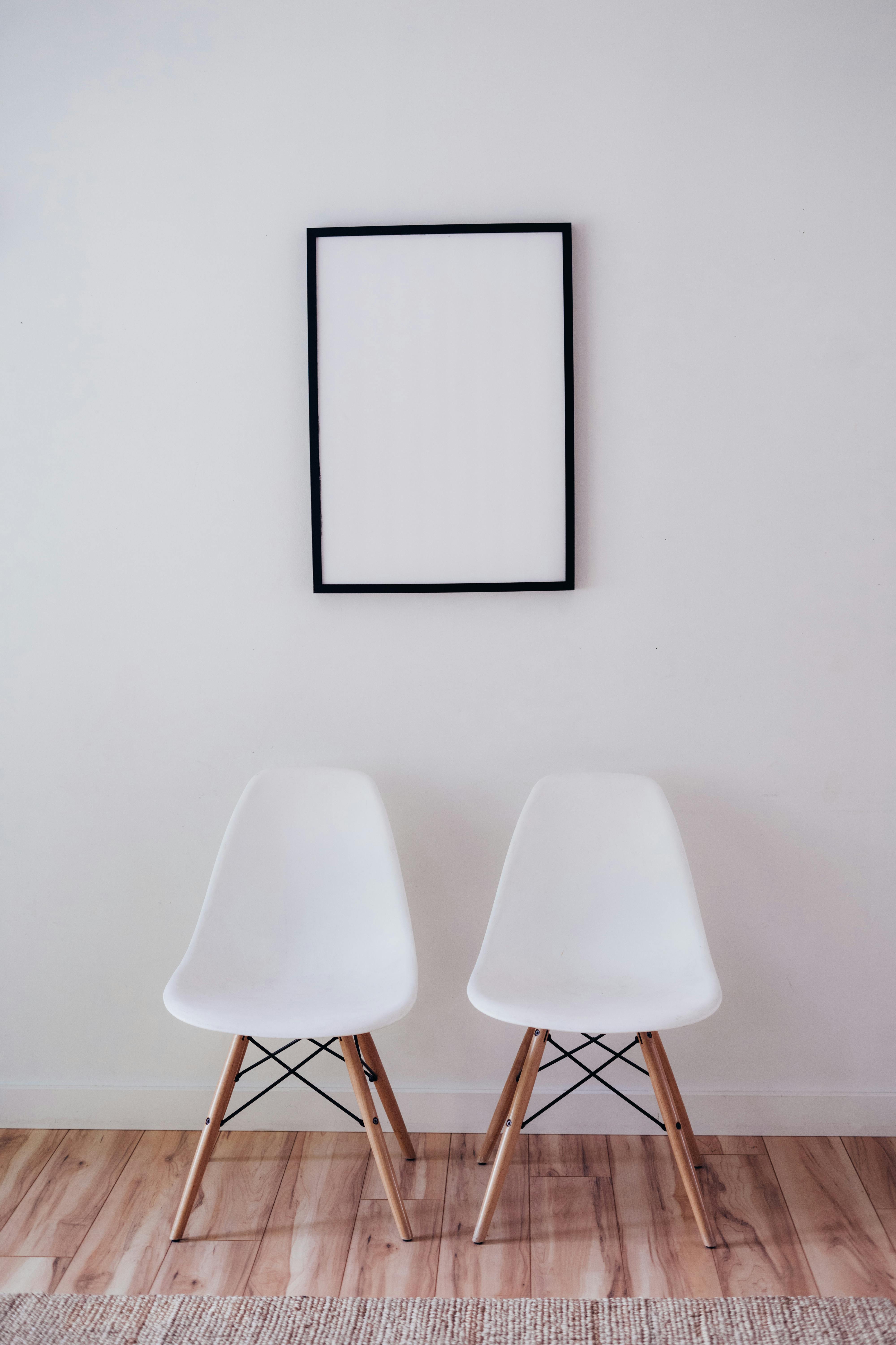 Minimalist interior with white chairs and an empty frame on the wall.