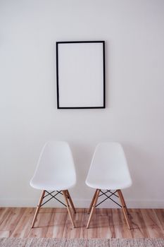 Minimalist interior with white chairs and an empty frame on the wall.