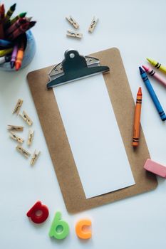 Flat lay of school supplies with a blank clipboard, crayons, and abc letters.