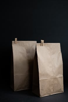 Vertical shot of two paper bags with wooden clips on a dark background, perfect for product mockups.