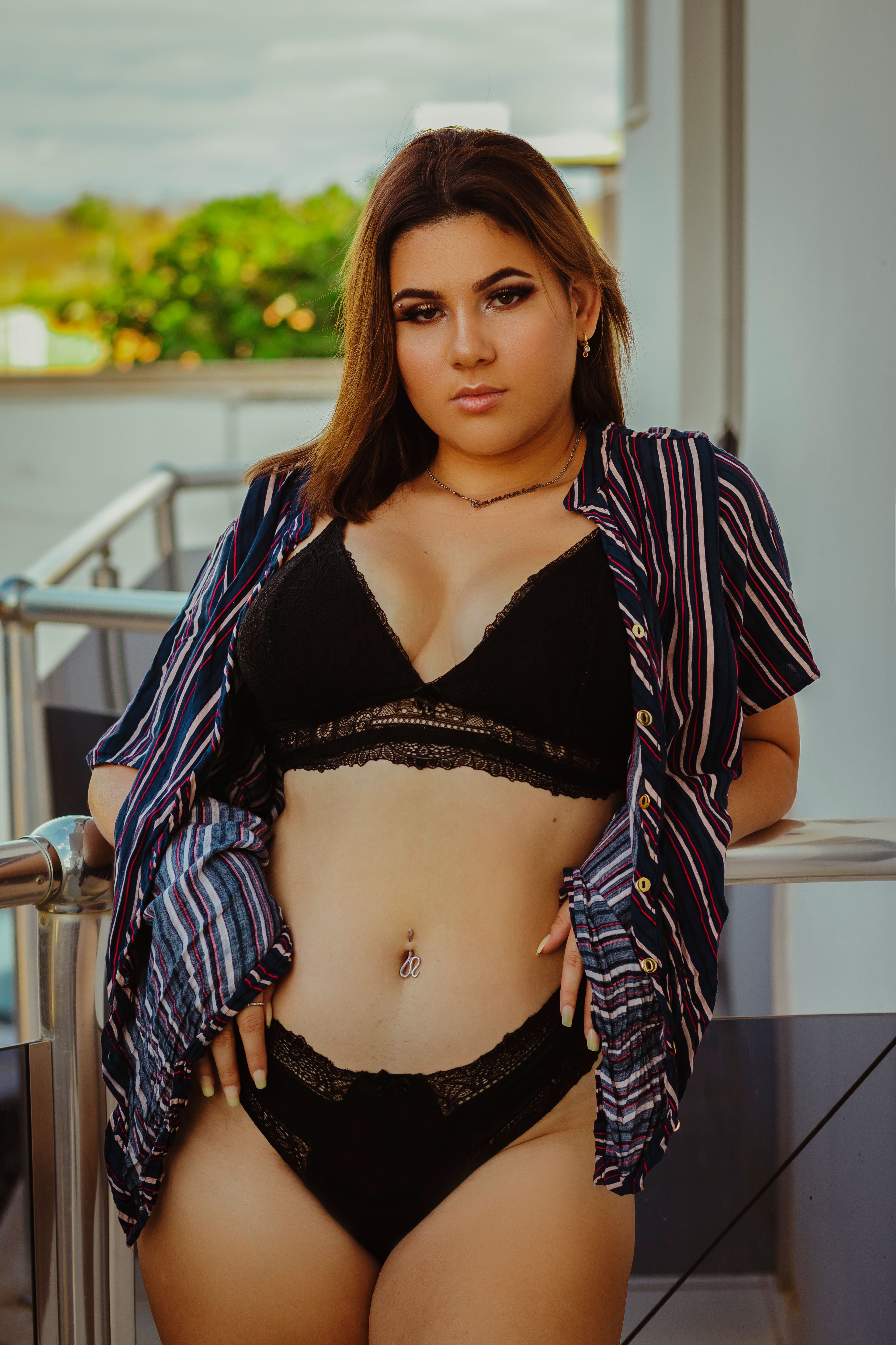 A confident woman in black lingerie poses on a balcony, embracing her natural beauty and style.