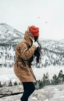 A woman in a brown jacket and red beanie explores snow-covered mountains.