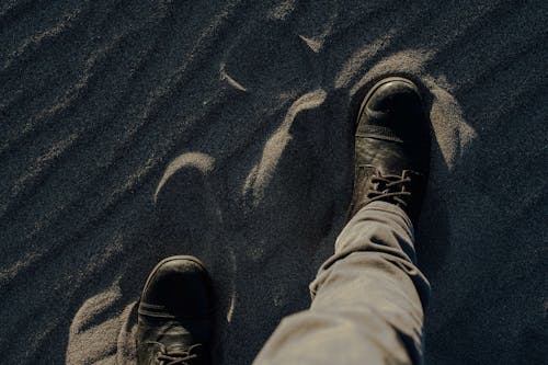 A Person Wearing Black Boots Standing on a Sandy Ground