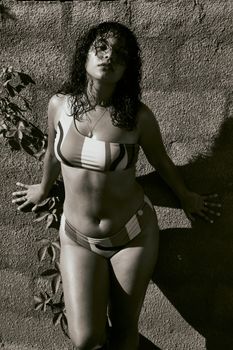 Artistic black and white portrait of a woman posing in a bikini against a textured wall.