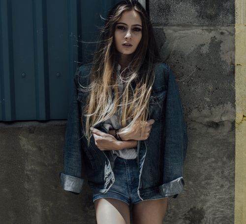 Free Fashionable woman in a denim jacket posing stylishly outdoors against a textured wall. Stock Photo