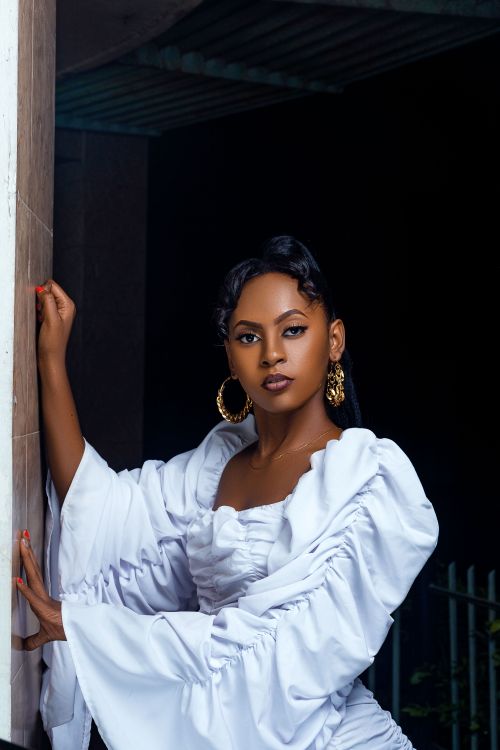 Free Stylish African American woman in a white dress with statement earrings, posing confidently. Stock Photo