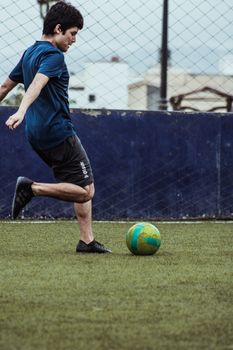 Young male soccer player in action on an outdoor field, kicking a colorful ball.