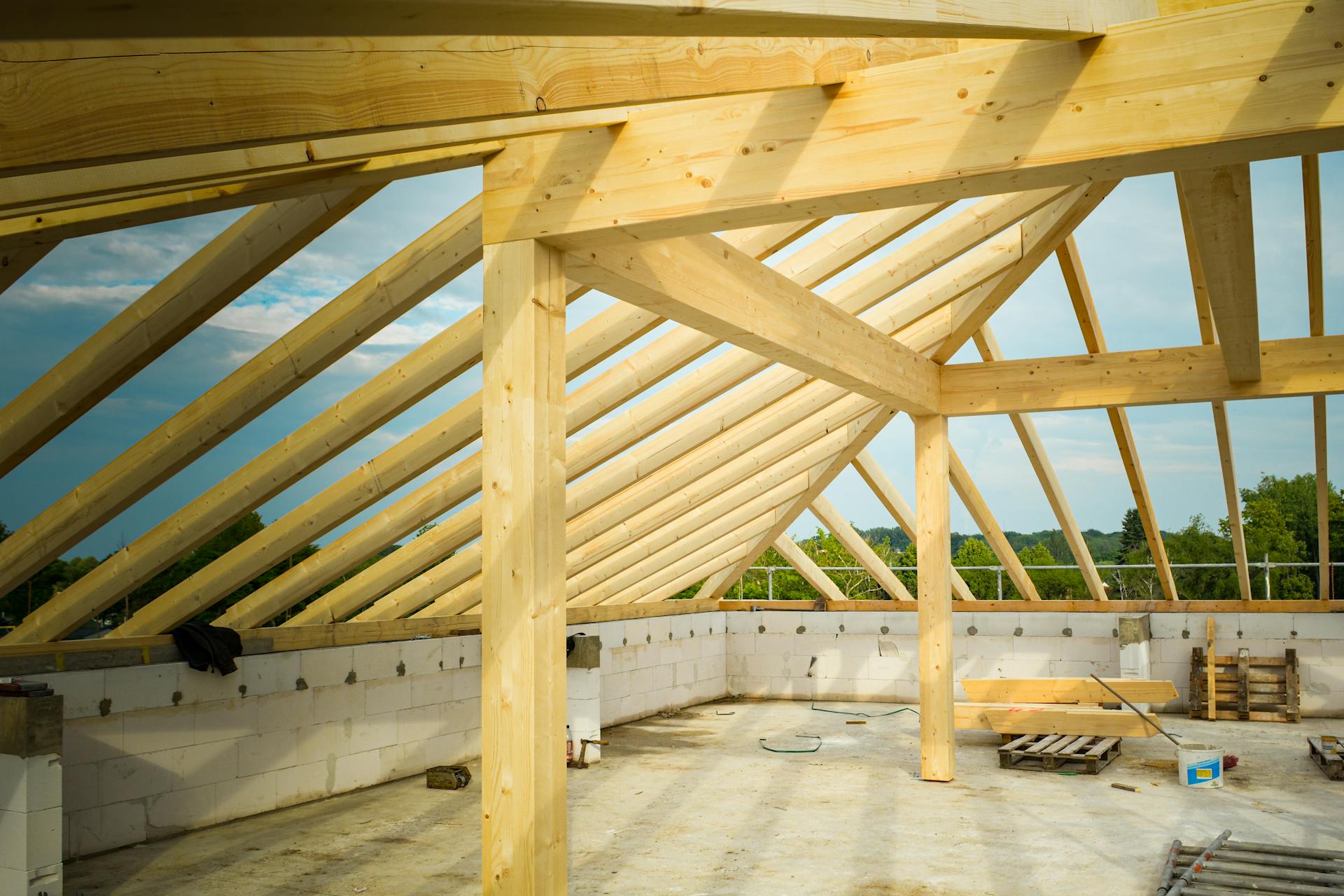 Unfinished construction site with a focus on wooden roof trusses under a clear sky.