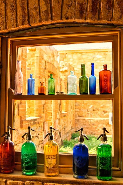 Free Colorful glass bottles displayed on a rustic window sill with a brick background. Stock Photo