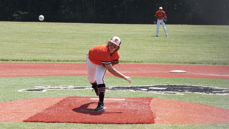Young baseball pitcher throwing a pitch during a game on an outdoor field.