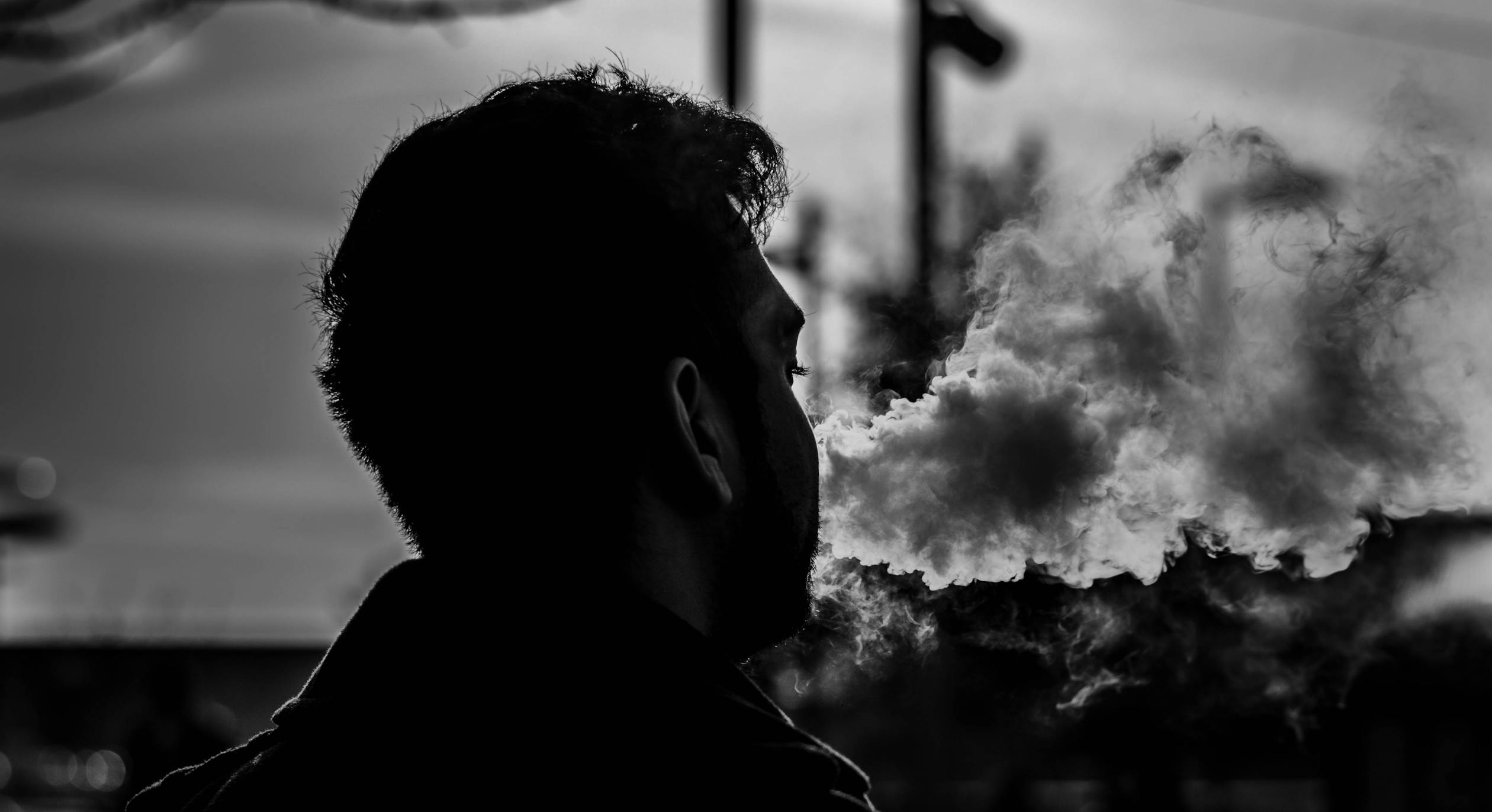 A close-up black and white photo of a young man vaping CBD.