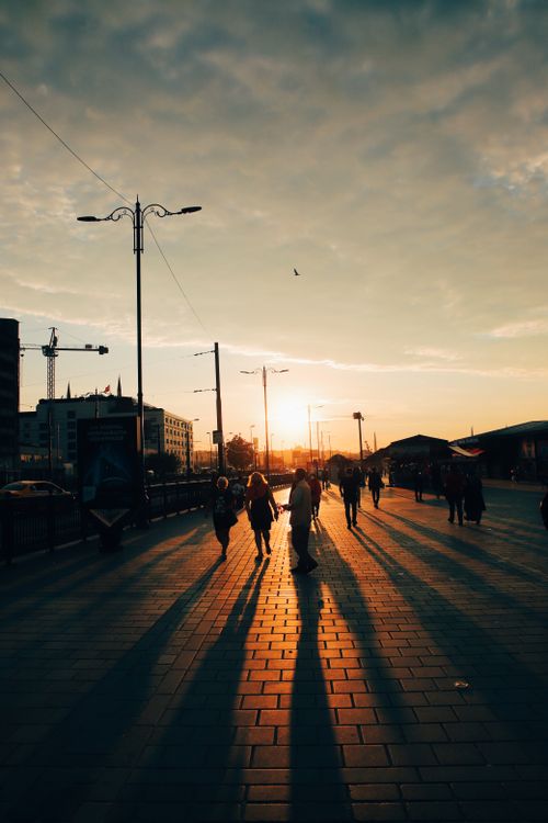 Free Silhouetted pedestrians on a city street during a dramatic sunset, casting long shadows. Stock Photo