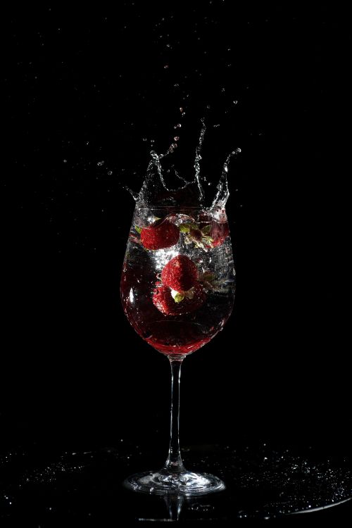 Free A dramatic shot of a raspberry cocktail splashing in a glass against a black background. Stock Photo