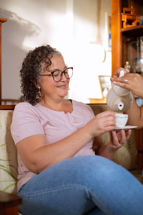 Free Smiling senior woman with curly hair enjoys tea indoors, adding warmth to a cozy setting. Stock Photo