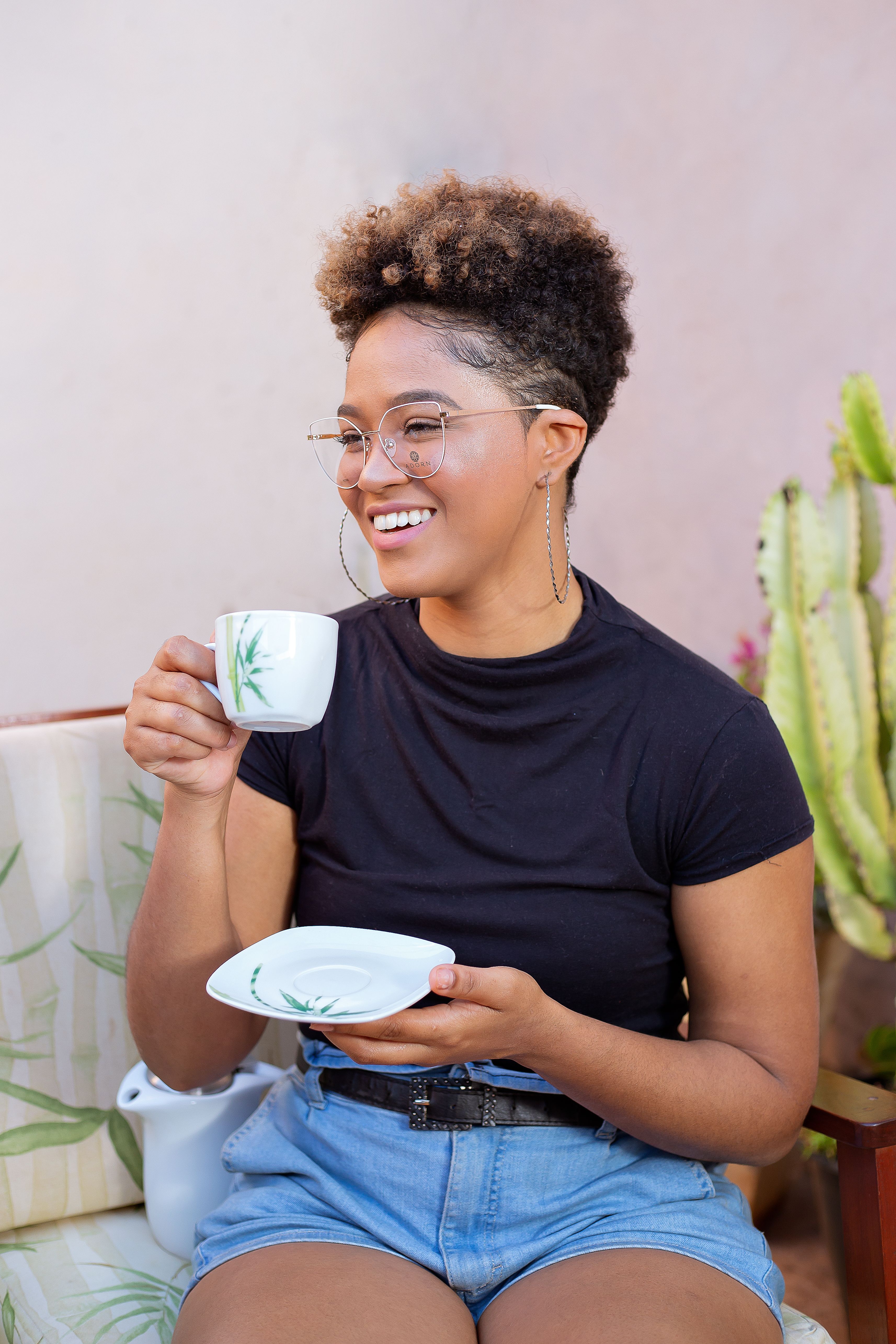 A cheerful young woman with curly hair enjoys coffee outdoors in a relaxed setting.