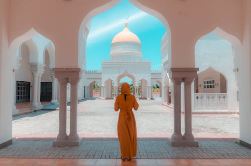Person in Orange Robe Standing Outside a Mosque