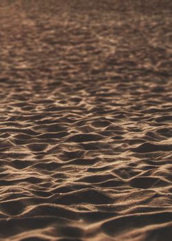 Sunset light casting shadows on textured sand for a serene beach scene.