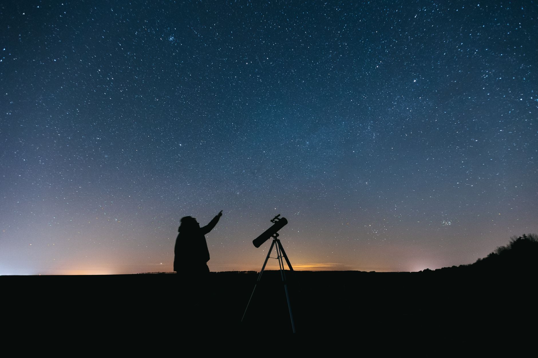 Silhouette of person with telescope gazing at a starry night sky, showcasing celestial beauty.